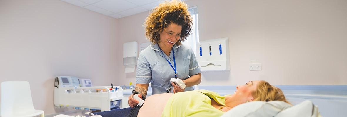 Eine Hebamme führt eine Ultraschalluntersuchung an einer schwangeren Frau durch.