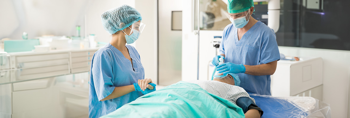 Eine operationstechnische Assistentin und ein anästhesietechnischer Assistent machen einen Patienten fertig zur Operation.