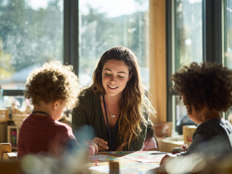 Eine Erzieherin in Ausbildung bastelt kreativ mit Kindern in der Kita als praxisorientierter Teil der frühkindlichen Bildung.