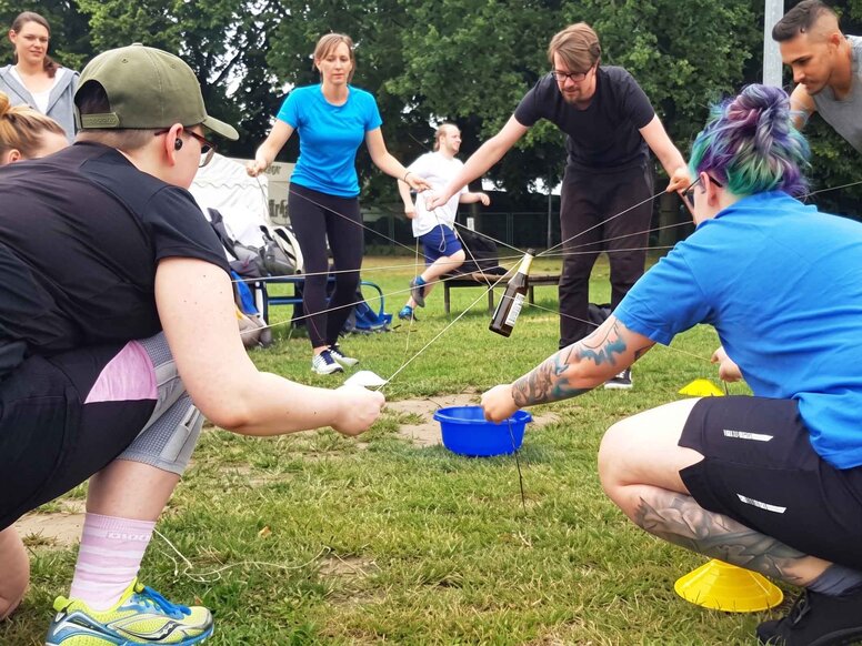 Gruppe bei einer kooperativen Teamchallenge auf einer Wiese. Mit Seilen und Werkzeugen wird gemeinsam eine Aufgabe zur Förderung von Kommunikation gelöst.
