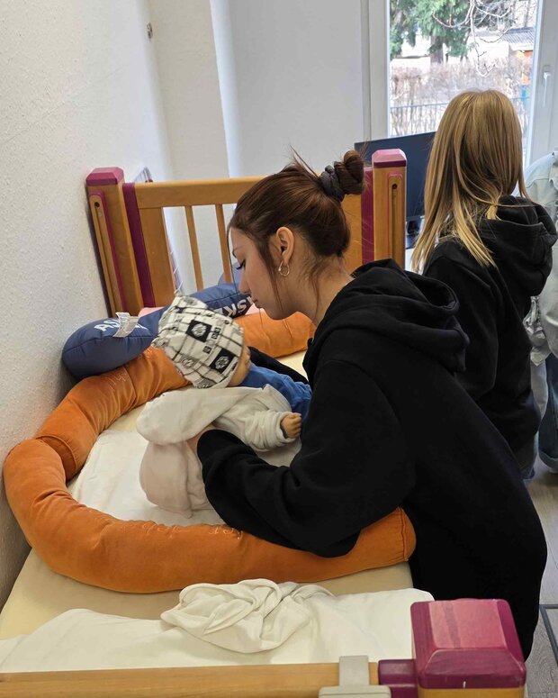 Lernende trainieren die Versorgung einer Babypuppe an einem Pflegebett in einem Schulungsraum.