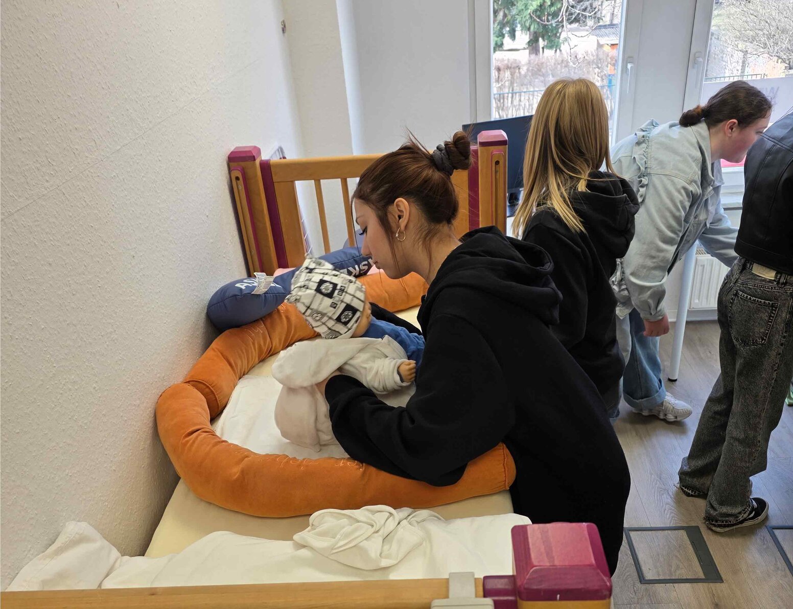 Lernende trainieren die Versorgung einer Babypuppe an einem Pflegebett in einem Schulungsraum.