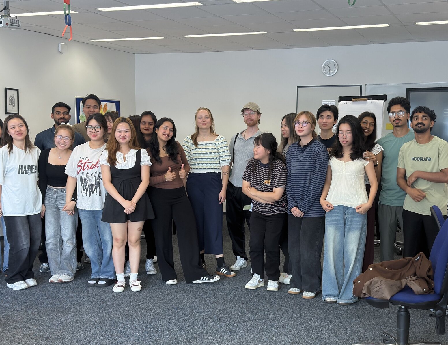 Klassenfoto von rund 20 Schüler:innen in einem Klassenraum mit Tischen, Whiteboard und Bildschirm.