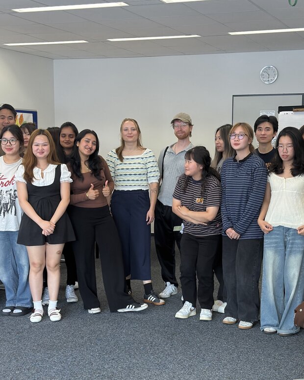 Klassenfoto von rund 20 Schüler:innen in einem Klassenraum mit Tischen, Whiteboard und Bildschirm.