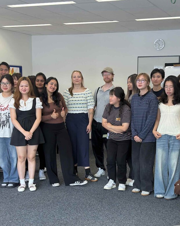 Klassenfoto von rund 20 Schüler:innen in einem Klassenraum mit Tischen, Whiteboard und Bildschirm.