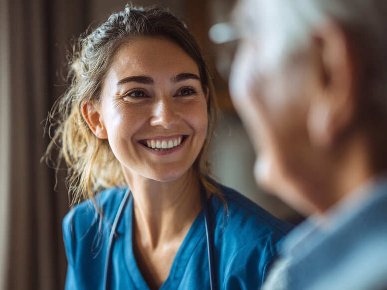 Portrait einer freundlichen Pflegeschülerin, die wertschätzend einen älteren Patienten anlächelt.