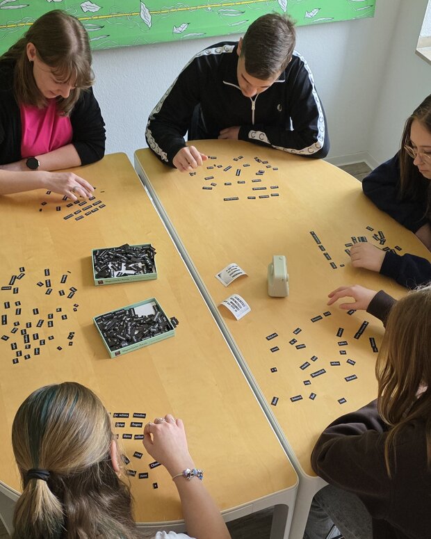 Sechs Schüler:innen bearbeiten an einem Tisch eine Aufgabe mit vielen Wortkärtchen.
