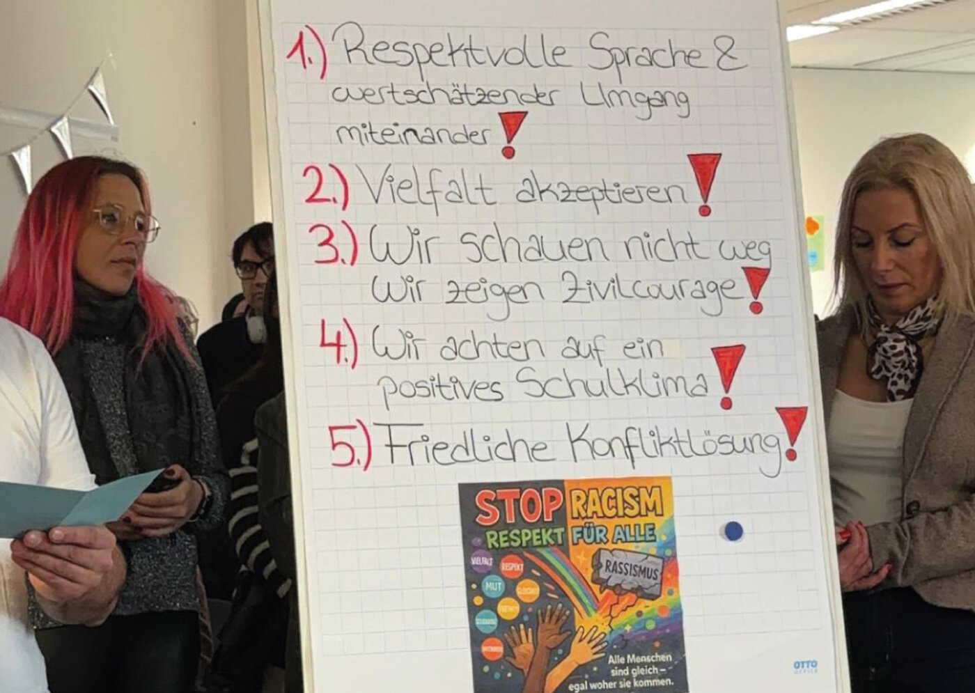 Schüler:innen präsentieren ihre Projektarbeit zum Thema Rassismus und zeigen ein Flipchart, auf dem sie gemeinsam erarbeitete Werte und Gedanken festgehalten haben.