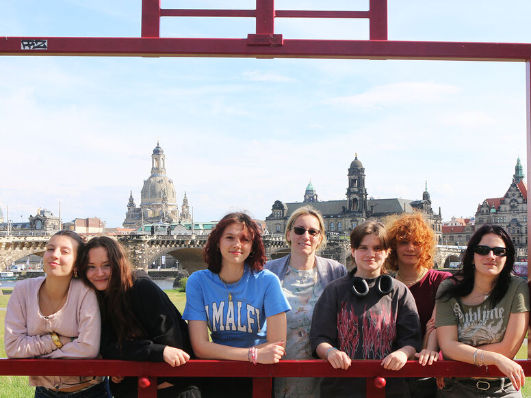 Sechs junge Frauen stehen während ihres Aufenthaltes mit Erasmus+ hinter einem großen roten Bilderrahmen auf einer Wiese, im Hintergrund die historische Altstadt von Dresden.