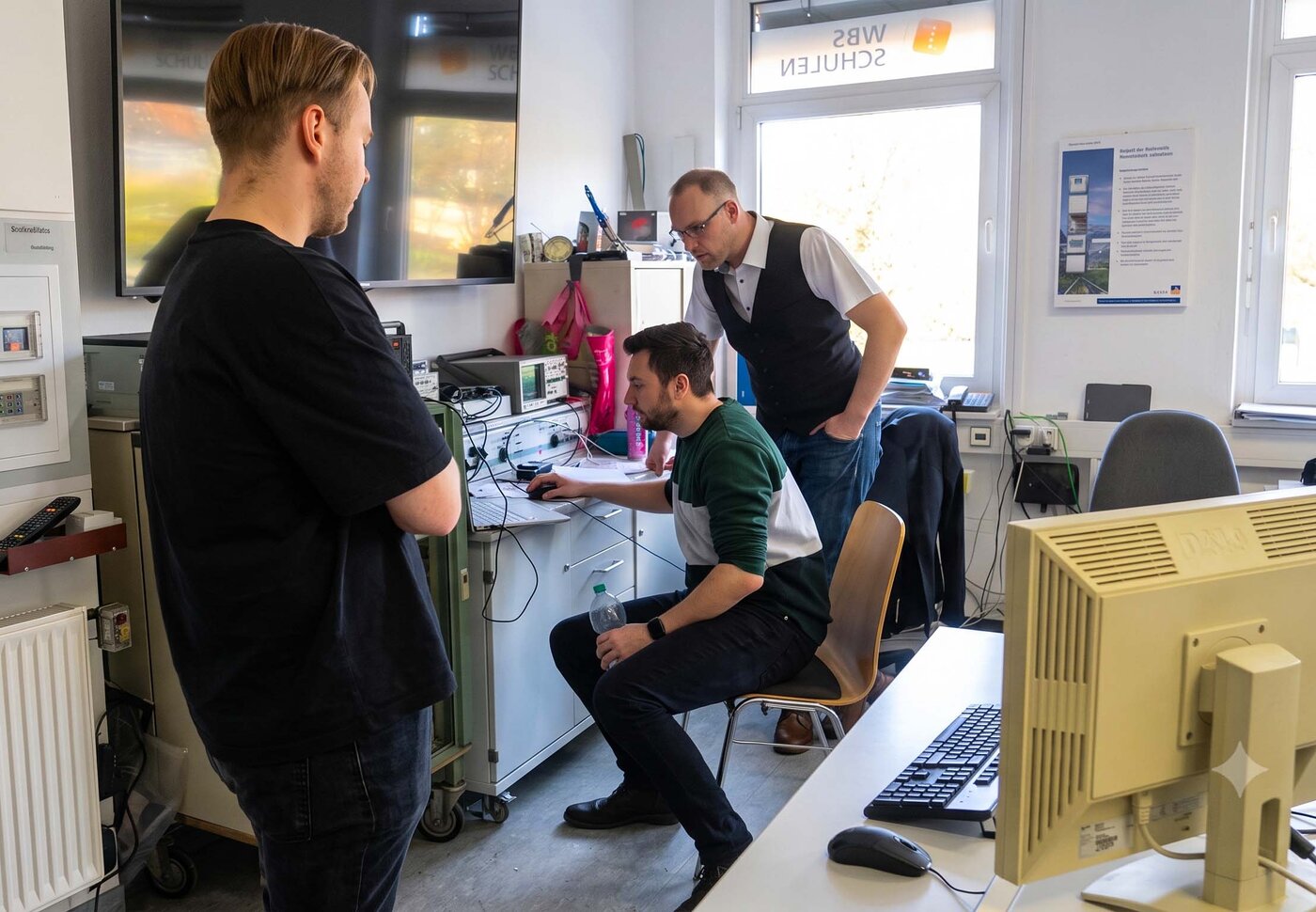 Studierende im Fachschulstudium Elektrotechnik in Leipzig arbeiten gemeinsam an einer Projektarbeit. In einem technisch ausgestatteten Labor analysieren und besprechen sie Messdaten und elektronische Systeme.
