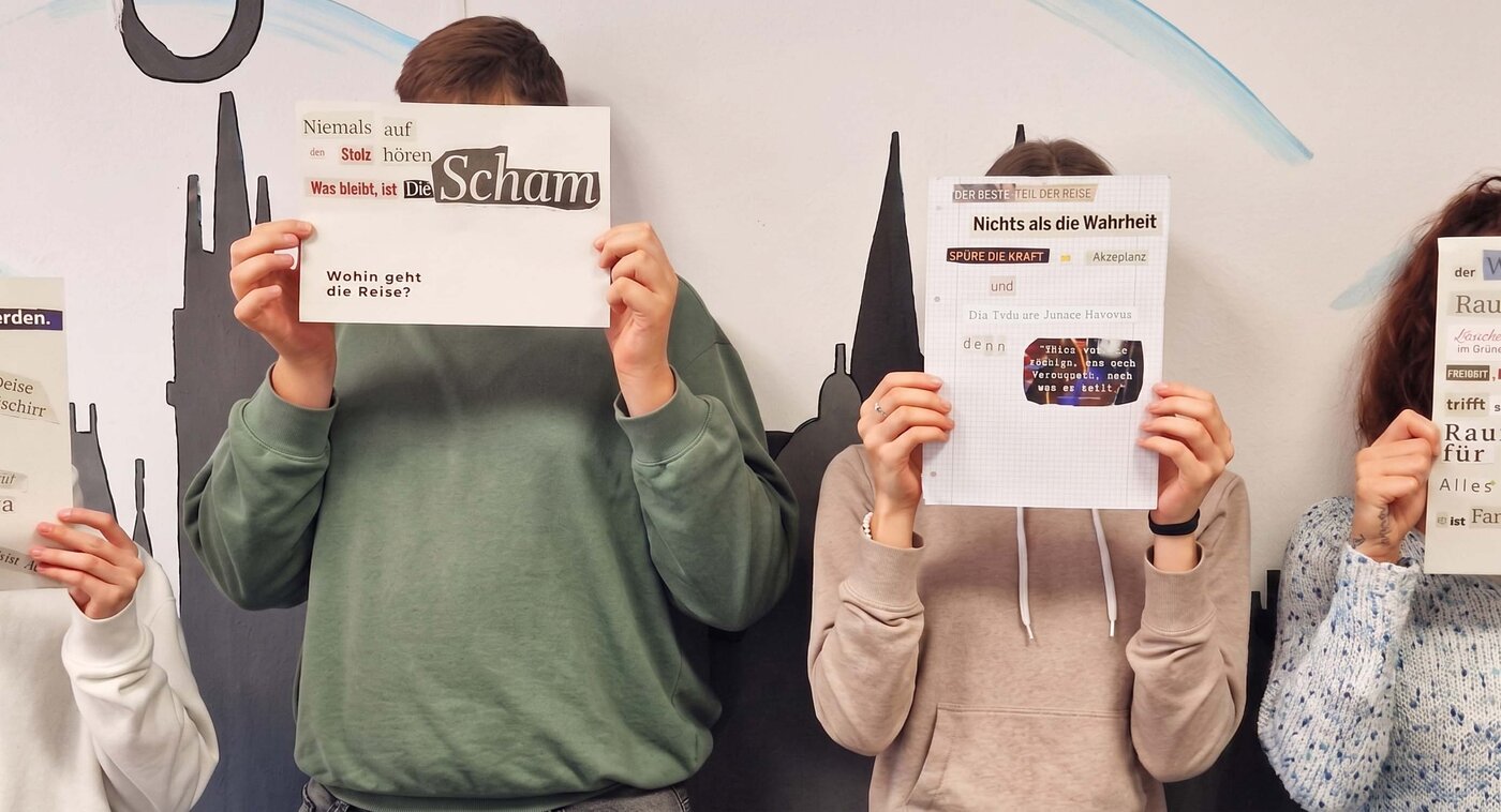 Vier Auszubildende stehen nebeneinander und verdecken ihre Gesichter mit selbstgestalteten Text-Collagen aus Zeitungsausschnitten, die sie in einem Workshop mit dem Thema Sprache erarbeitet haben.