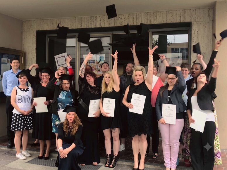 Eine Gruppe von feiernden Lernenden und Lernbegleiter:innen und Lernbegleiterinnen steht vor dem Eingang eines Schulgebäudes. 