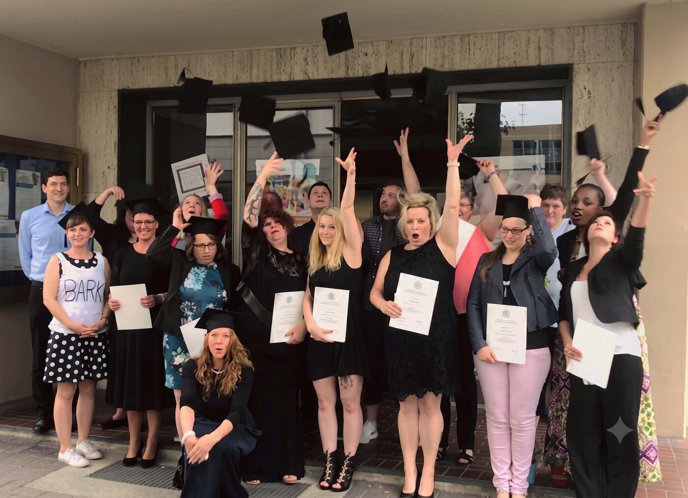 Eine Gruppe von feiernden Lernenden und Lernbegleiter:innen und Lernbegleiterinnen steht vor dem Eingang eines Schulgebäudes. 