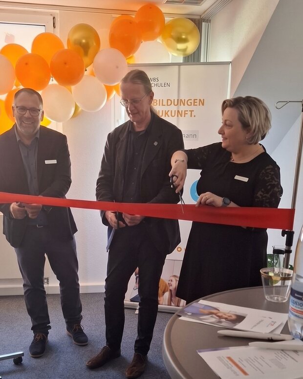 Banddurchschnitt zur Eröffnung eines Bildungsstandorts WBS SCHULEN Ilmenau vor einer Dekoration aus orange-weißen Luftballons.