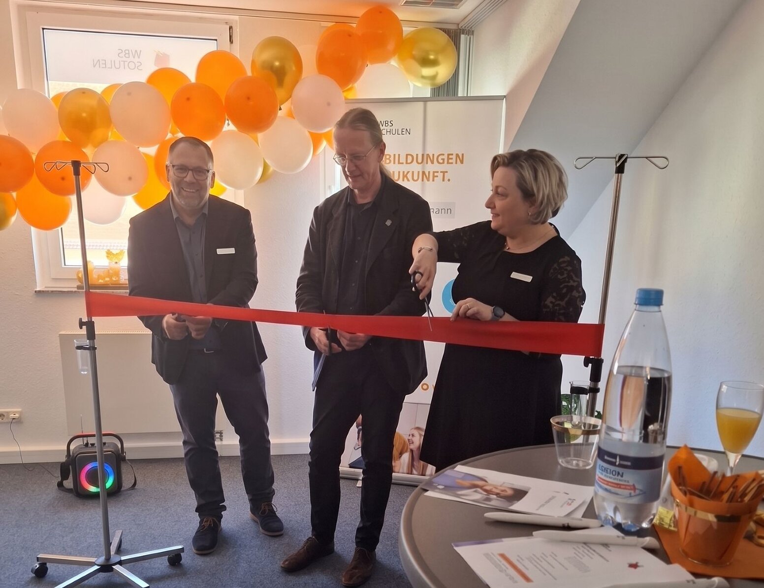 Banddurchschnitt zur Eröffnung eines Bildungsstandorts WBS SCHULEN Ilmenau vor einer Dekoration aus orange-weißen Luftballons.