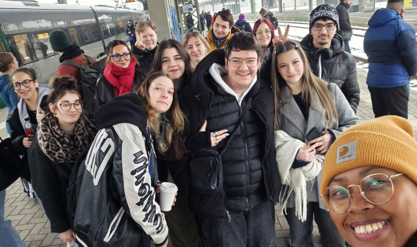 Fröhliches Gruppen-Selfie von Schülern bei einer Exkursion zu den Körperwelten an einem Bahnhof. 