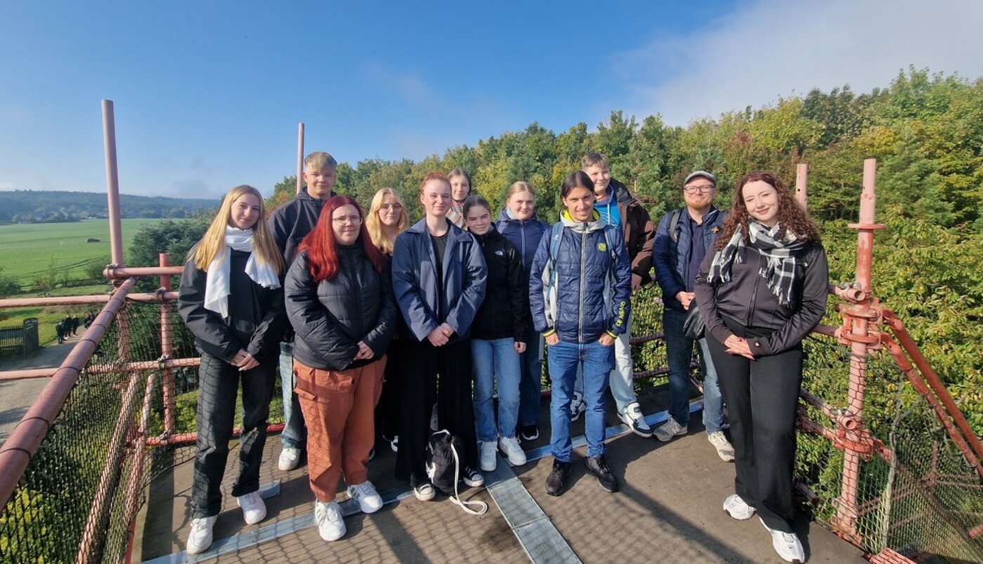 Gruppenbild angehender Sozialassistent:innen während eines Wandertags in und um Tharandt. Die Gruppe steht auf einer Aussichtsplattform, umgeben von Natur, Feldern und bewaldeten Hügeln.
