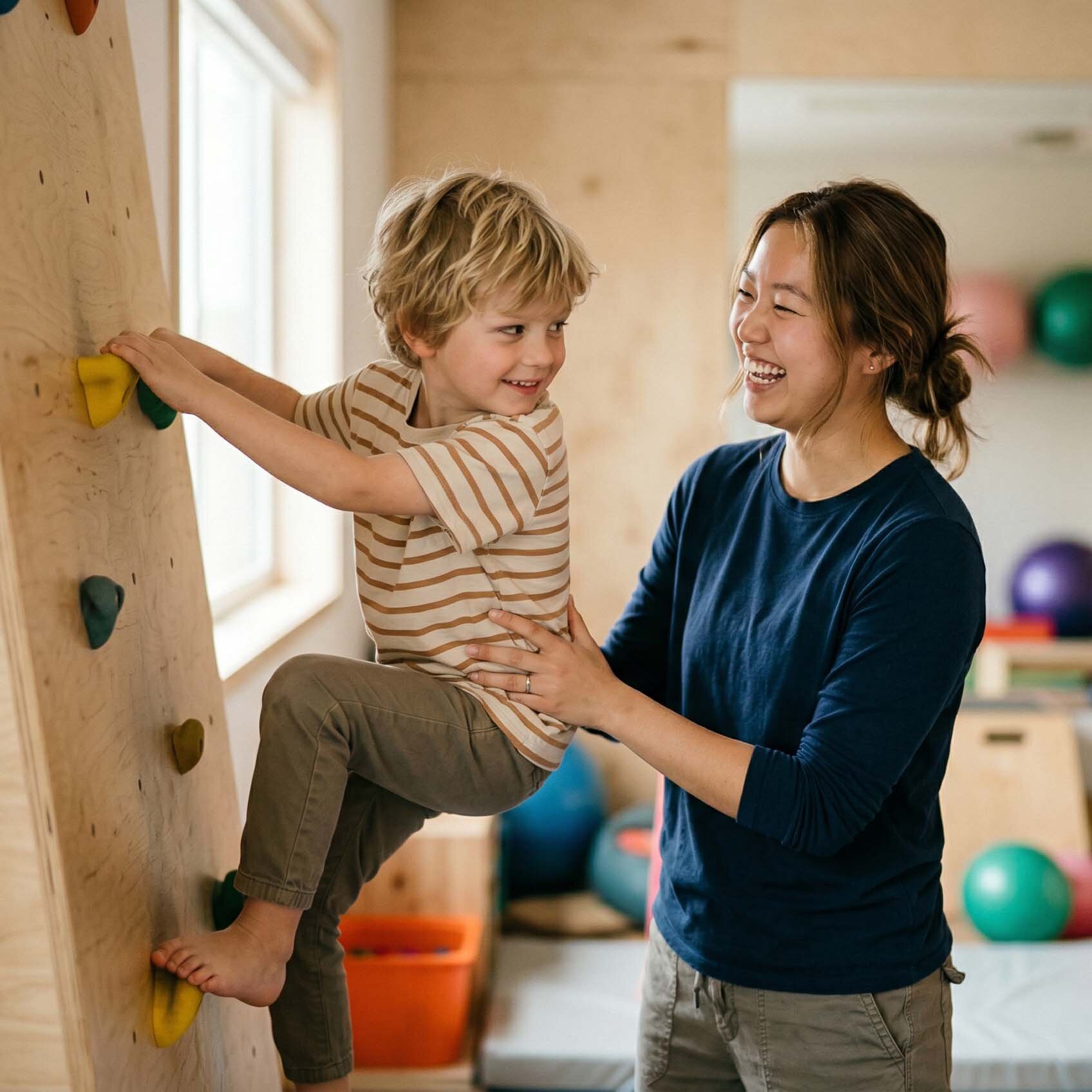 Eine Auszubildende zur Erzieherin sichert lachend einen Jungen beim Klettern an einer Kletterwand im Sportraum einer Kindertagesstätte.