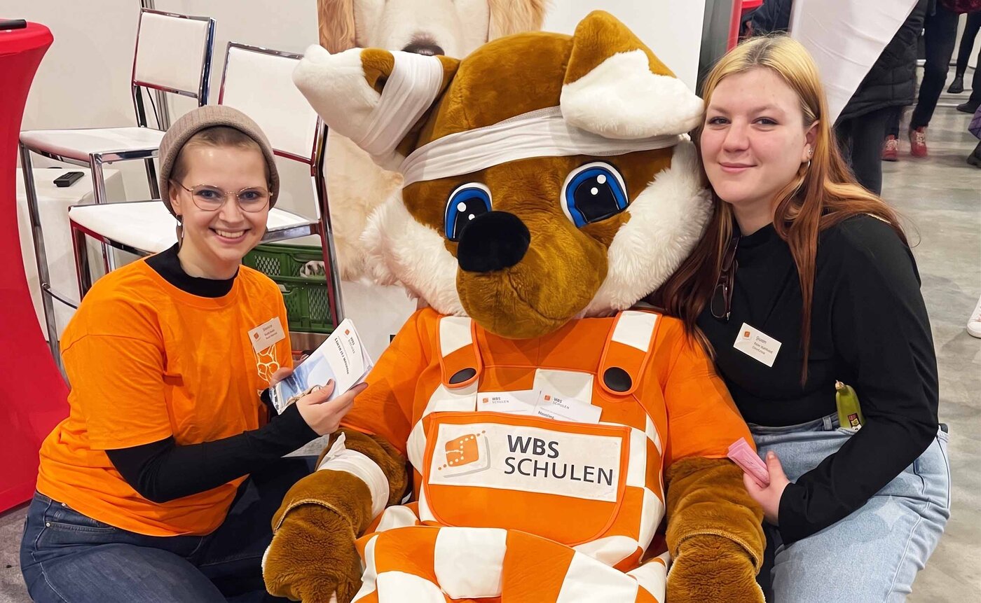 Zwei junge Auszubildende posieren lächelnd mit Schlaufuchs, der Verbände am Kopf trägt, auf der Chancen-Messe in Halle. 