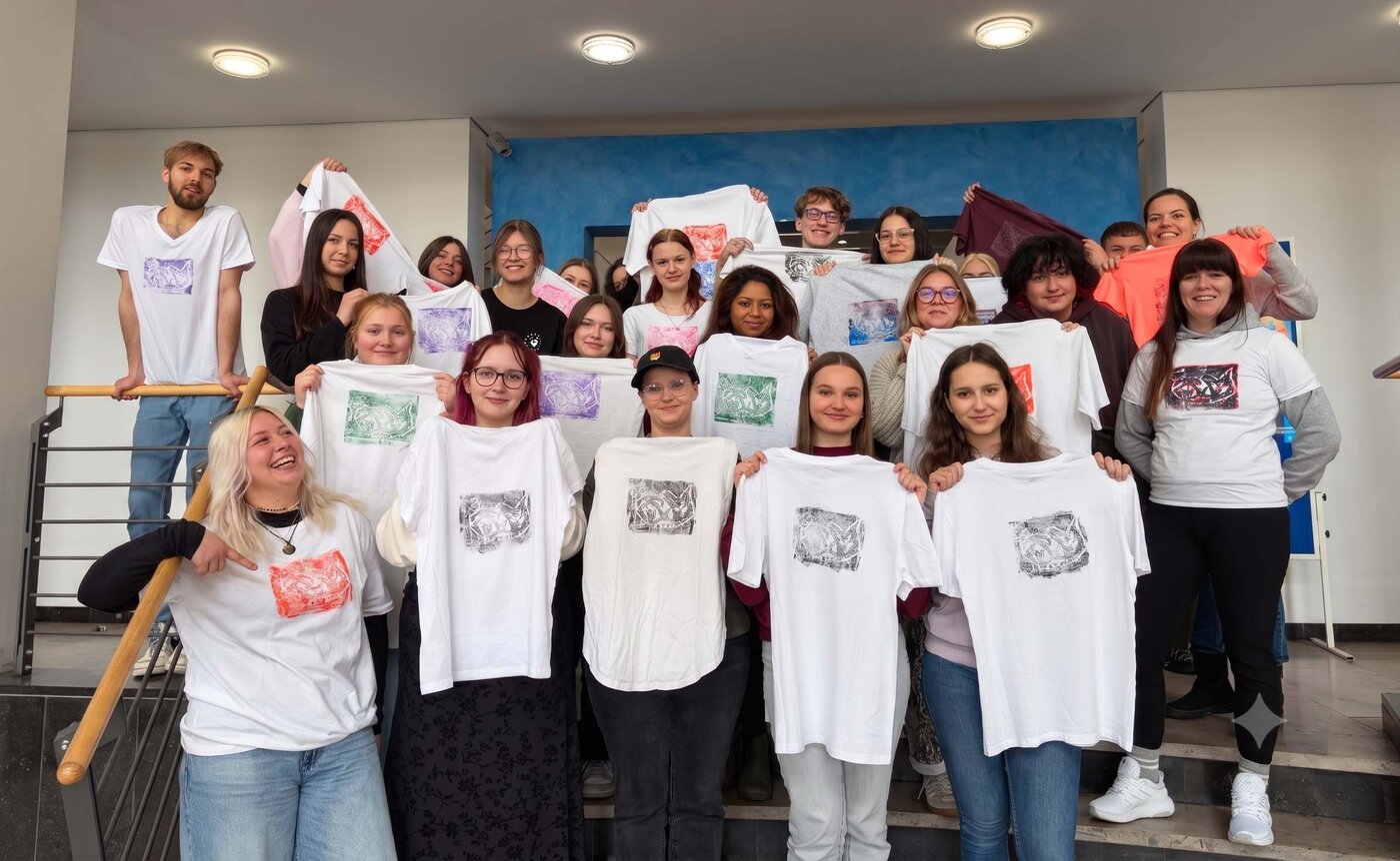 Auszubildende in Halle präsentieren selbst gestaltete T-Shirts aus einem kreativen Textildruckprojekt. Die Gruppe zeigt die Ergebnisse gemeinsamer künstlerischer Arbeit und individueller Gestaltung.
