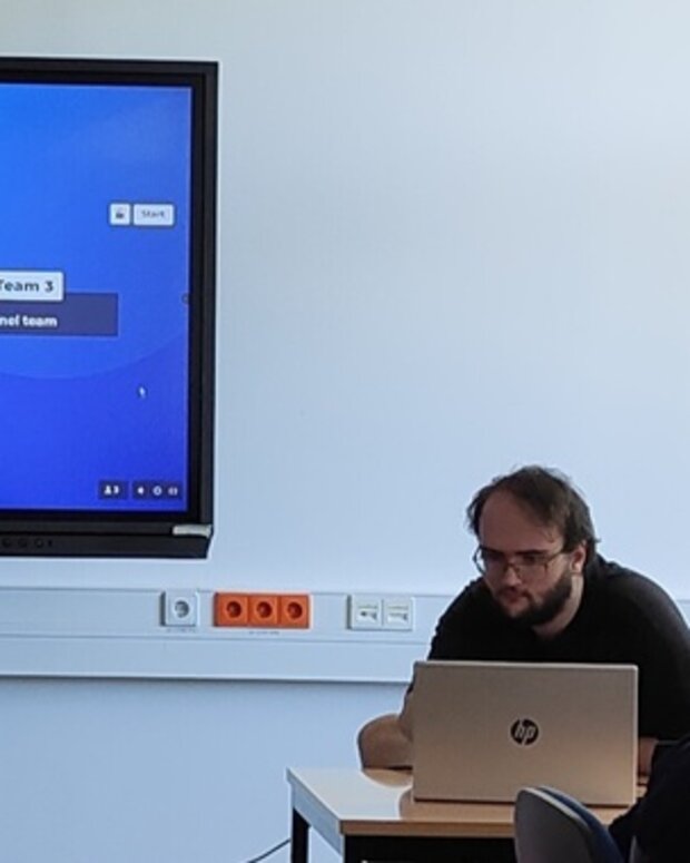 Kahoot-Quiz auf einem Bildschirm in einem Seminarraum, daneben ein Schüler am Laptop.