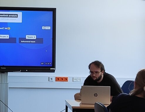 Kahoot-Quiz auf einem Bildschirm in einem Seminarraum, daneben ein Schüler am Laptop.