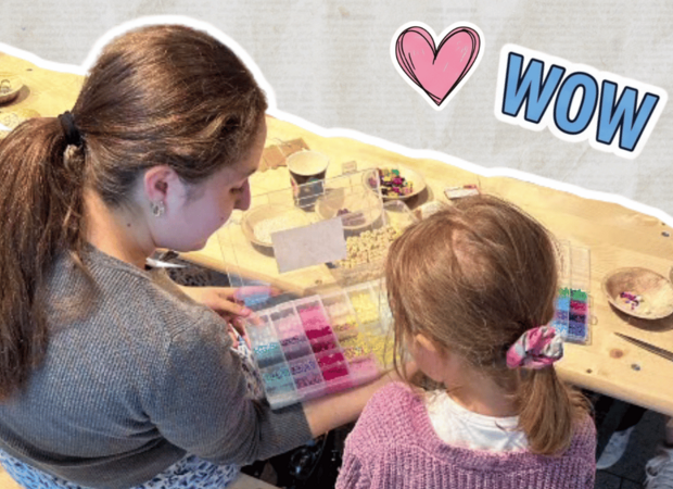 Freigestellte Fotocollage von zwei Personen an einem Basteltisch. Eine Person zeigt einer weiteren Person eine Sortierbox mit bunten Bastelmaterialien. Auf dem Tisch liegen verschiedene Schalen und kreative Materialien. Dekorative Sticker mit einem Herz und dem Schriftzug „WOW“ ergänzen das Motiv.