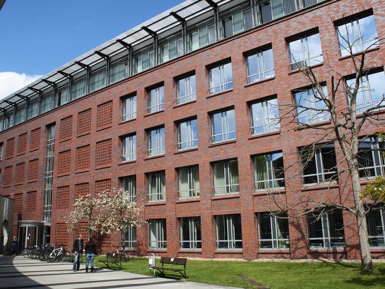 Außenansicht des Standortes der WBS SCHULEN Halle in der Franckestraße 15 in Halle (Saale) eines modernen, mehrstöckigen Backsteingebäudes. Im Vordergrund stehen zwei Personen auf einem gepflasterten Weg neben Grünflächen.