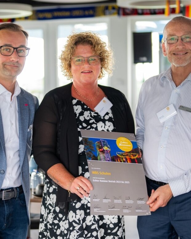 Mitarbeitende der WBS SCHULEN und offizielle Vertretungen der Initiative „Echter Hammer Betrieb“ präsentieren gemeinsam die Auszeichnungsurkunde „Echter Hammer Betrieb“ bei einer Veranstaltung. Die Urkunde wird in die Kamera gehalten.