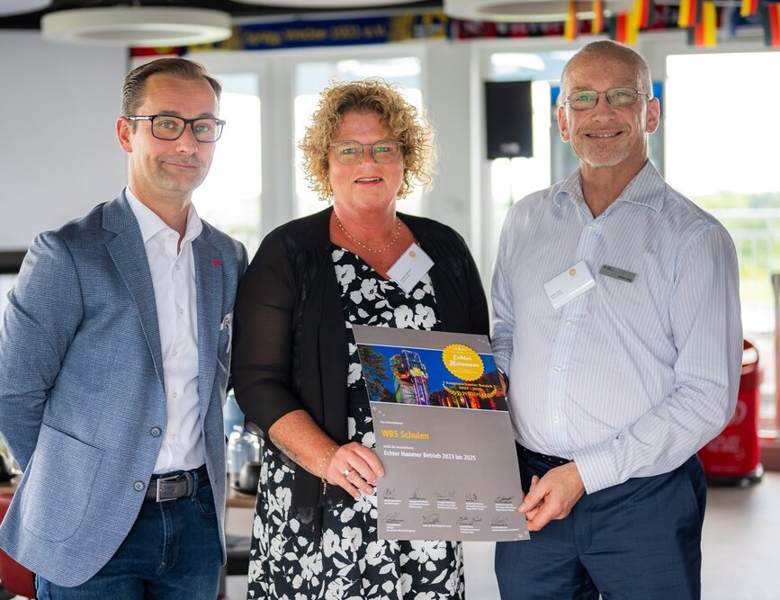 Mitarbeitende der WBS SCHULEN und offizielle Vertretungen der Initiative „Echter Hammer Betrieb“ präsentieren gemeinsam die Auszeichnungsurkunde „Echter Hammer Betrieb“ bei einer Veranstaltung. Die Urkunde wird in die Kamera gehalten.