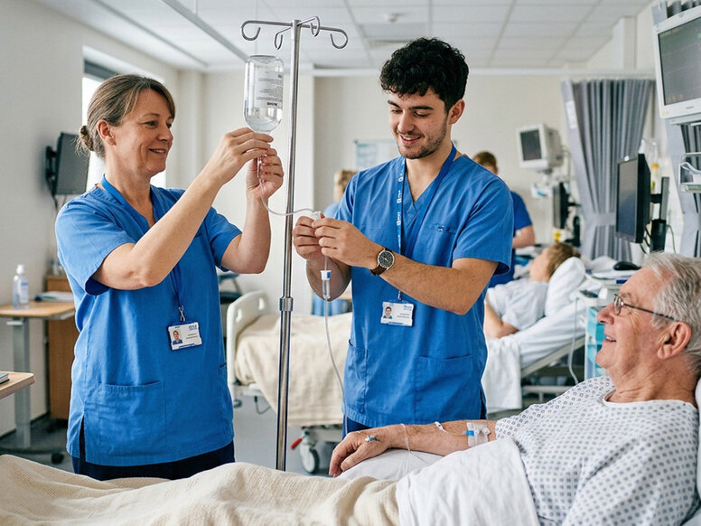 Erfahrene Pflegefachkraft und Pflegefachassistent bereiten lächelnd am Bett eines älteren Patienten eine Infusion vor.
