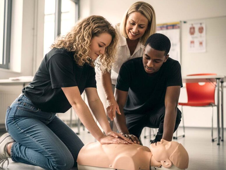 Zwei Auszubildende zum Notfallsanitäter üben handlungsorientiert die Reanimation an einer Torsopuppe unter Anleitung im Praxistraining.