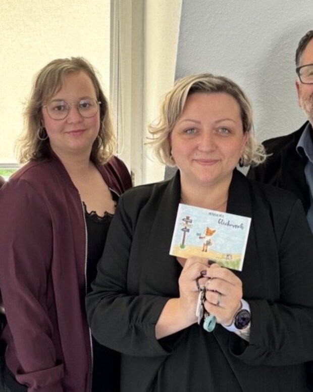 Gruppenfoto vom Schulteam in der Schule Ilmenau; die Person in der Mitte präsentiert eine kleine illustrierte Karte zur Eröffnung des neuen Standortes in Ilmenau.