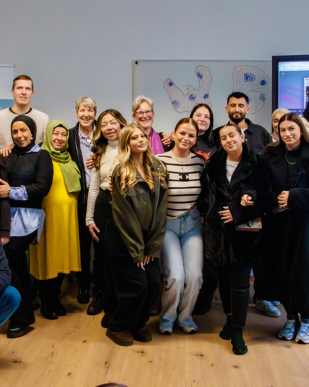 Gruppenfoto in einem Klassenraum: Rund 20 Absolvent:innen der Sozialassistenz-Ausbildung in Berlin stehen und sitzen vor einer Wand. Auf dem Roll-up links steht „WBS SCHULEN“, einige Zeichnungen hängen an der Wand.