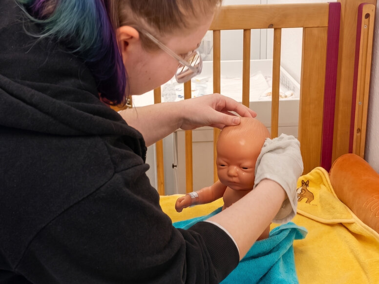 Pflegeschülerin übt das Waschen eines Säuglings an einer Babypuppe im Ausbildungsraum.