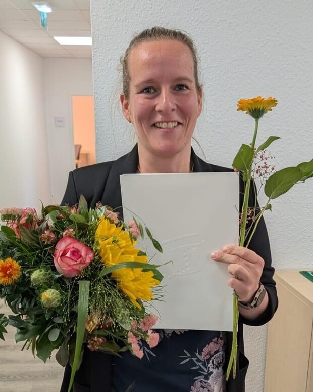 Absolventin mit Urkunde und Blumenstrauß nach erfolgreichem Ausbildungsabschluss.