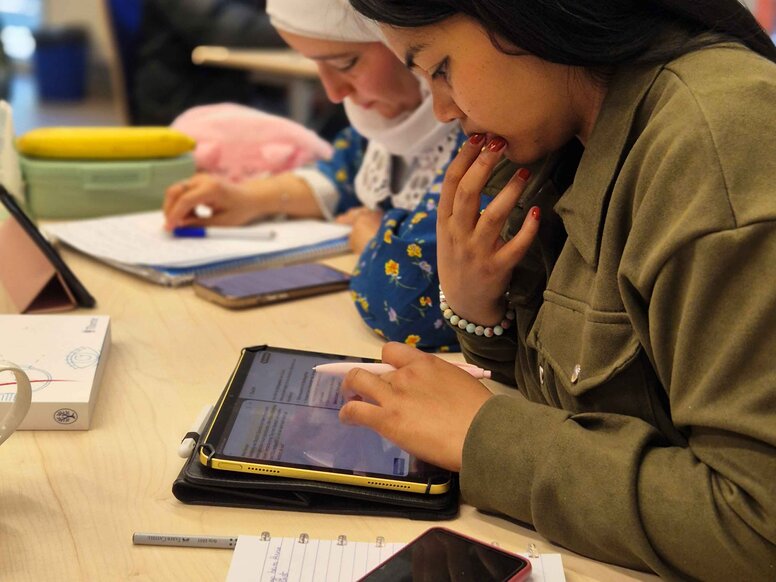 Zwei Lernende sitzen an einem Tisch im Rahmen des Unterrichtskonmzepts SOL (selbstorganisiertes Lernen). Eine Person liest auf einem Tablet mit Eingabestift, die andere macht handschriftliche Notizen. Vor ihnen liegen Lernmaterialien und ein Smartphone.