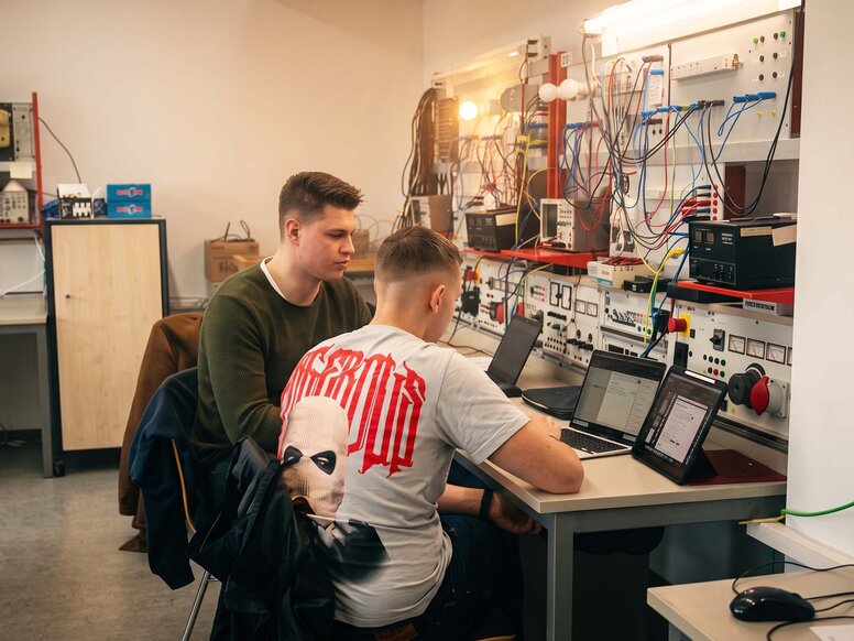 Studierende des Fachschulstudiums Elektrotechnik in Leipzig bearbeiten Aufgaben am Laptop. Der Unterricht findet in einem Labor mit Schaltungen, Messgeräten und technischen Versuchsständen statt.