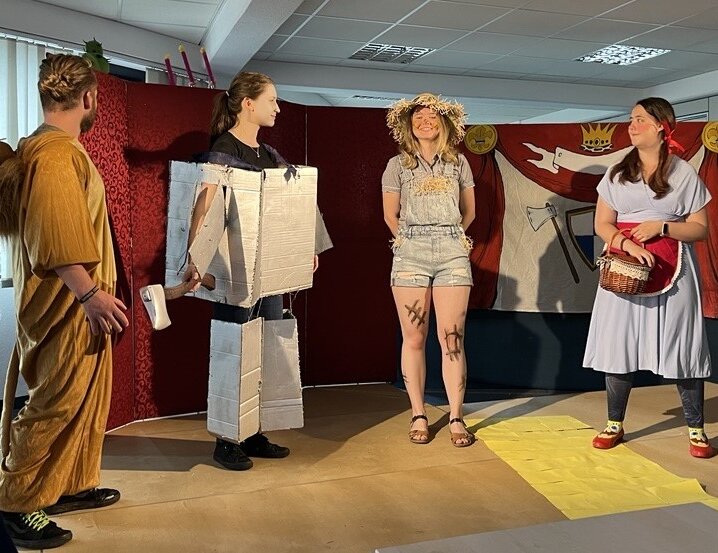 Theateraufführung mit vier kostümierten Schuler:innen auf einer Bühne vor einer gestalteten Kulisse.