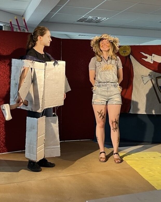 Theateraufführung mit vier kostümierten Schuler:innen auf einer Bühne vor einer gestalteten Kulisse.