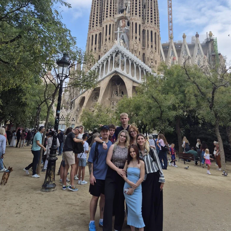 Mehrere Teilnehmende eines Auslandspraktikums posieren für ein Gruppenfoto auf dem Vorplatz der Sagrada Família in Barcelona. Im Hintergrund ist die berühmte Basilika mit ihren hohen Türmen und der charakteristischen Architektur von Antoni Gaudí zu sehen.