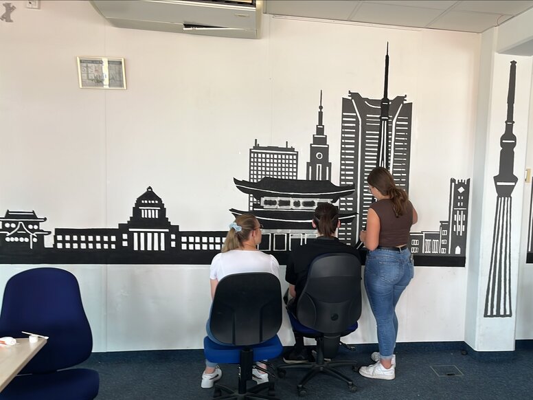 Schüler arbeiten in einem Seminarraum vor einer selbst gestalteten Wand mit Stadtsilhouette der Stadt Tokio.