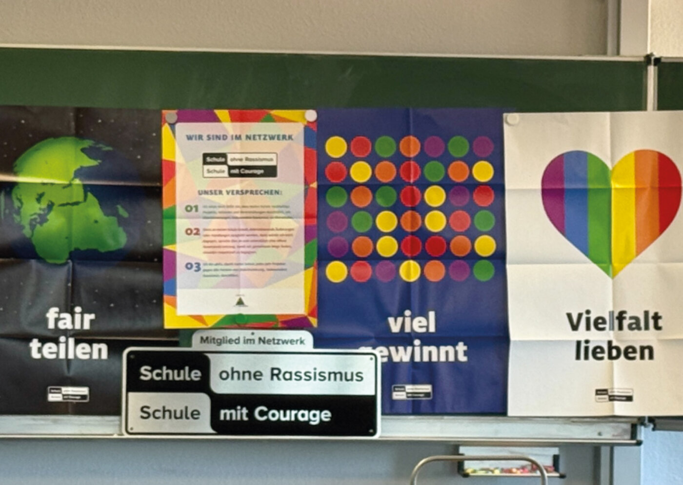 Plakate zum Thema Vielfalt hängen an einer Tafel neben dem Siegel „Schule ohne Rassismus – Schule mit Courage“ in einer Schule in Dresden.