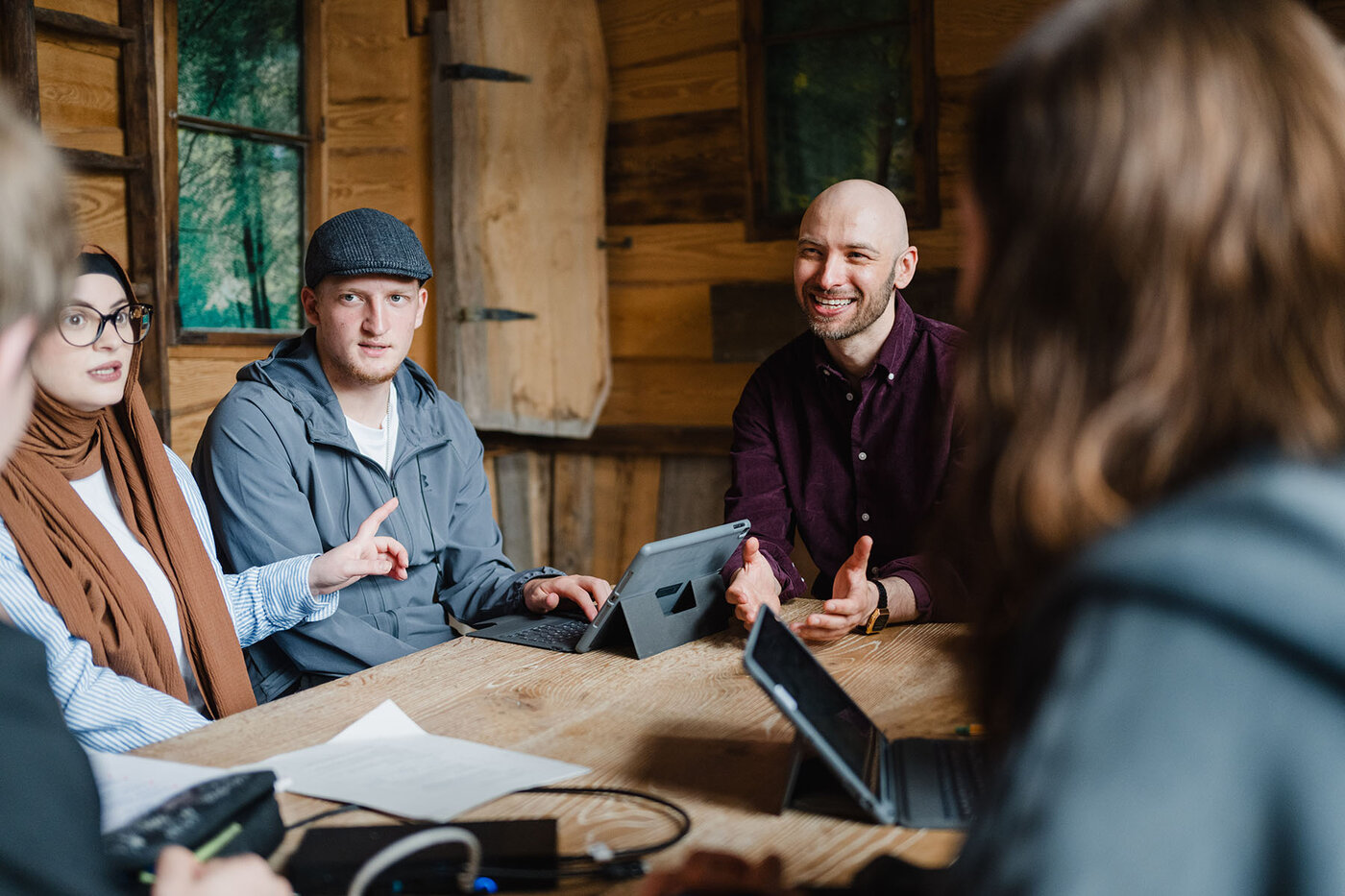 Ein Lernbegleiter unterstützt eine Gruppe Auszubildender bei ihrer Gruppenarbeit im Baumhaus genannten Raum