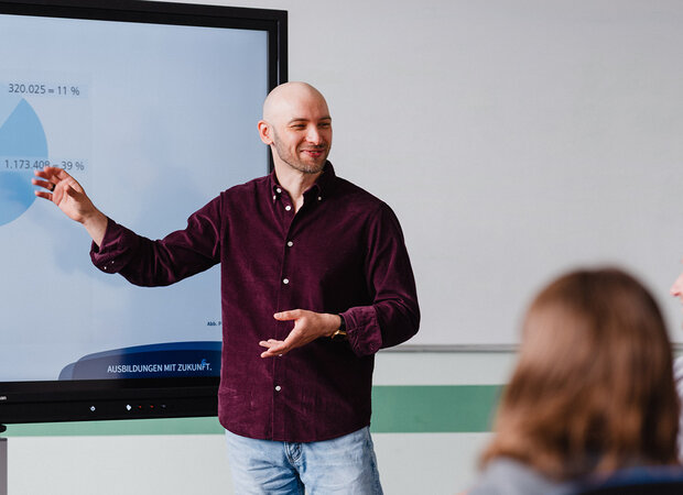 Ein Lehrer steht am digitalen Whiteboard und gibt einen fachlichen Input für die Auszubildenden in der Pflege