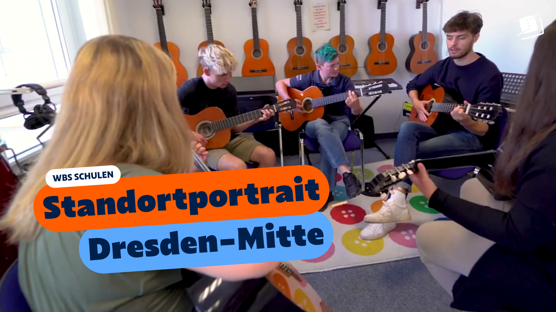 Mehrere Personen sitzen im Kreis in einem Musikraum und spielen gemeinsam Gitarren. An der Wand hängen weitere Gitarren. Eingeblendeter Text: „WBS SCHULEN – Standortportrait Dresden-Mitte“.