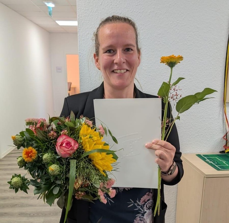 Absolventin mit Urkunde und Blumenstrauß nach erfolgreichem Ausbildungsabschluss.