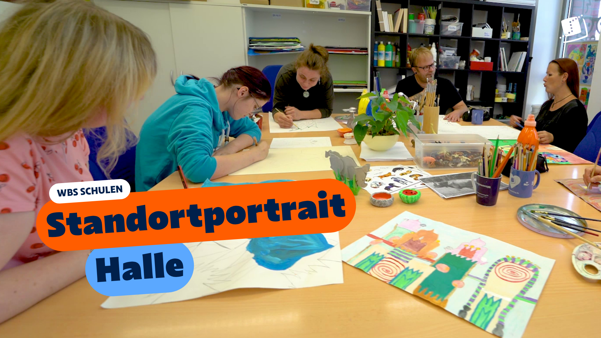 Zwei Personen sitzen an einem Tisch in einem Unterrichtsraum und betrachten gemeinsam ein anatomisches Handmodell. Eingeblendeter Text: „WBS SCHULEN – Standortportrait Plauen“.