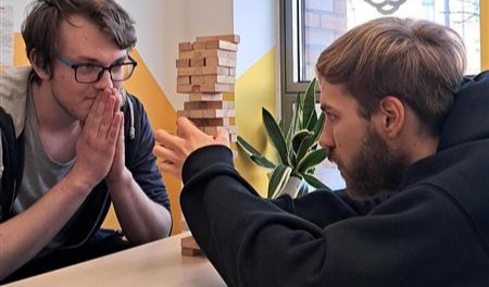Zwei Schüler konzentrieren sich auf einen Turm aus Holzklötzen bei einem Geschicklichkeitsspiel.