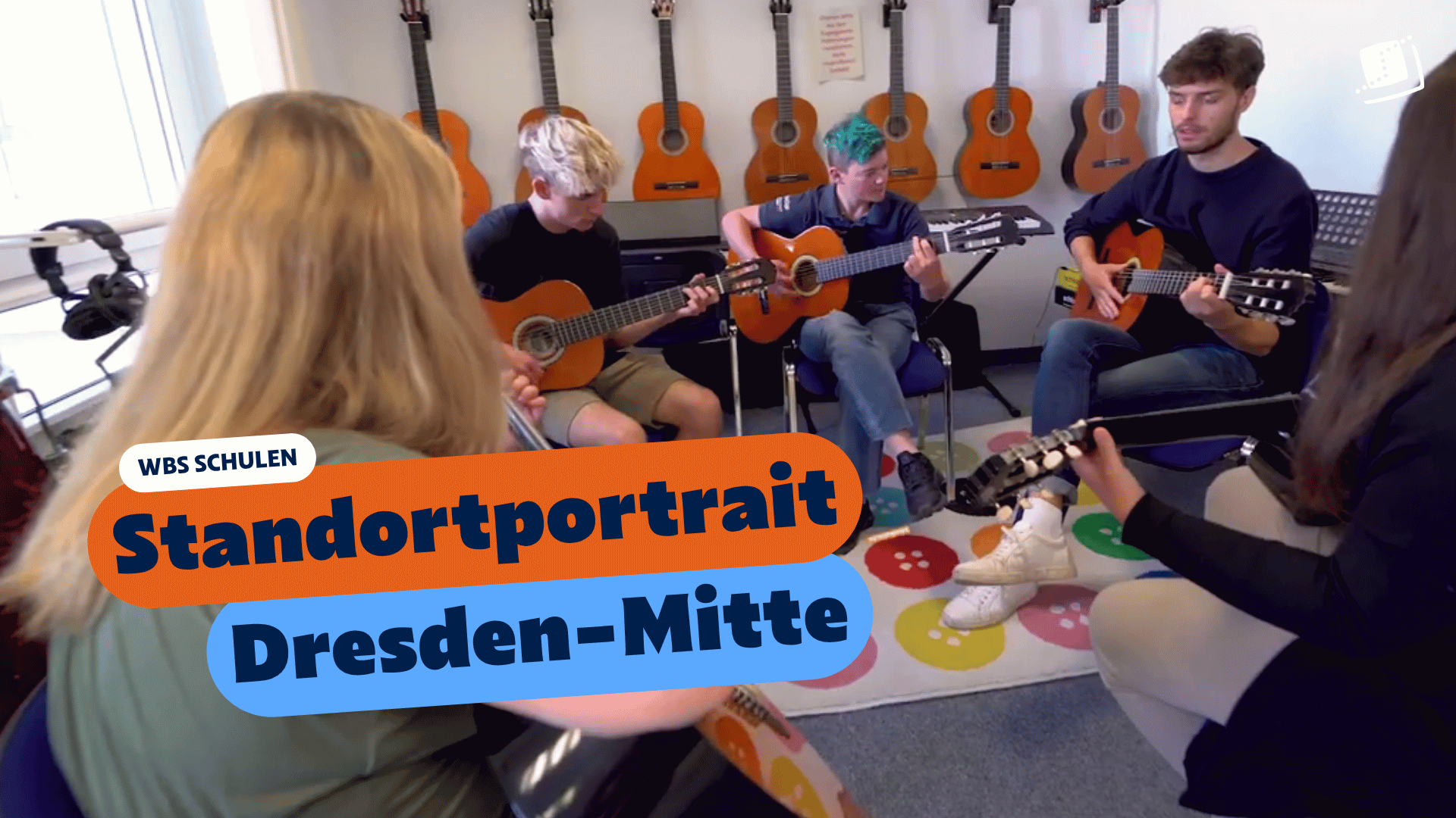 Mehrere Personen sitzen im Kreis in einem Musikraum und spielen gemeinsam Gitarren. An der Wand hängen weitere Gitarren. Eingeblendeter Text: „WBS SCHULEN – Standortportrait Dresden-Mitte“.